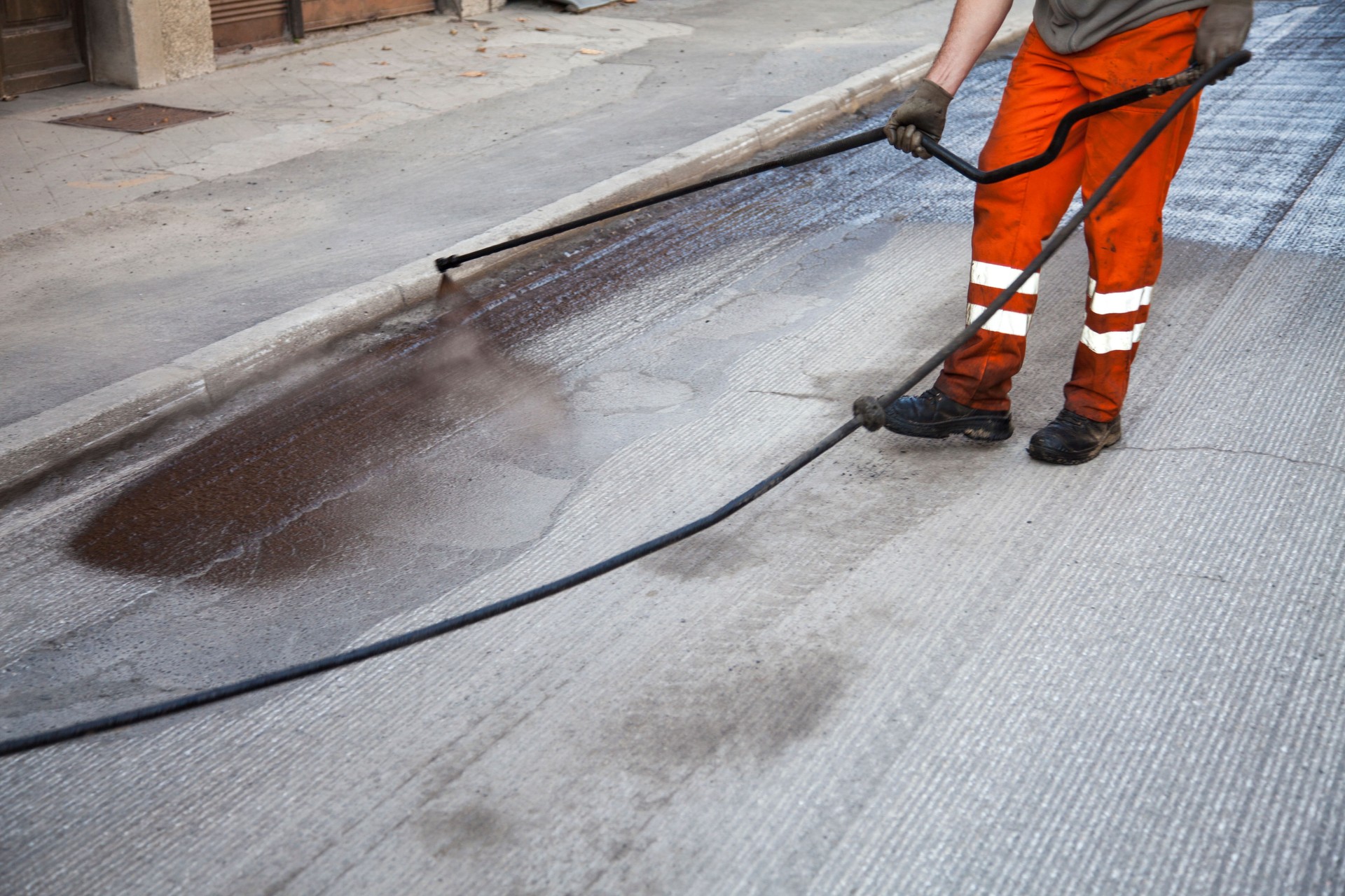 Worker spraying asphalt sealer