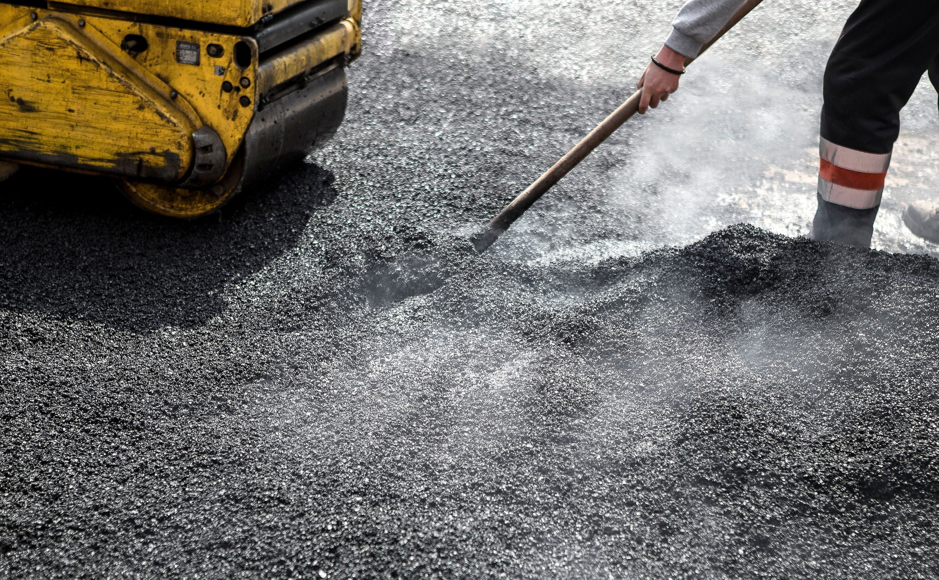 Worker with roller compacting asphalt on a road fixing pothole