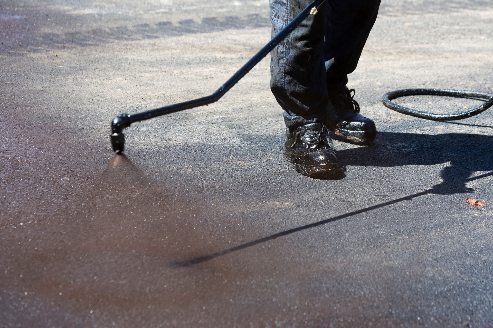 Worker spraying hot asphalt professionally asphalt sealing a parking lot